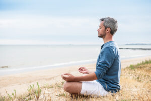 Man sitting on beach doing yoga breathing