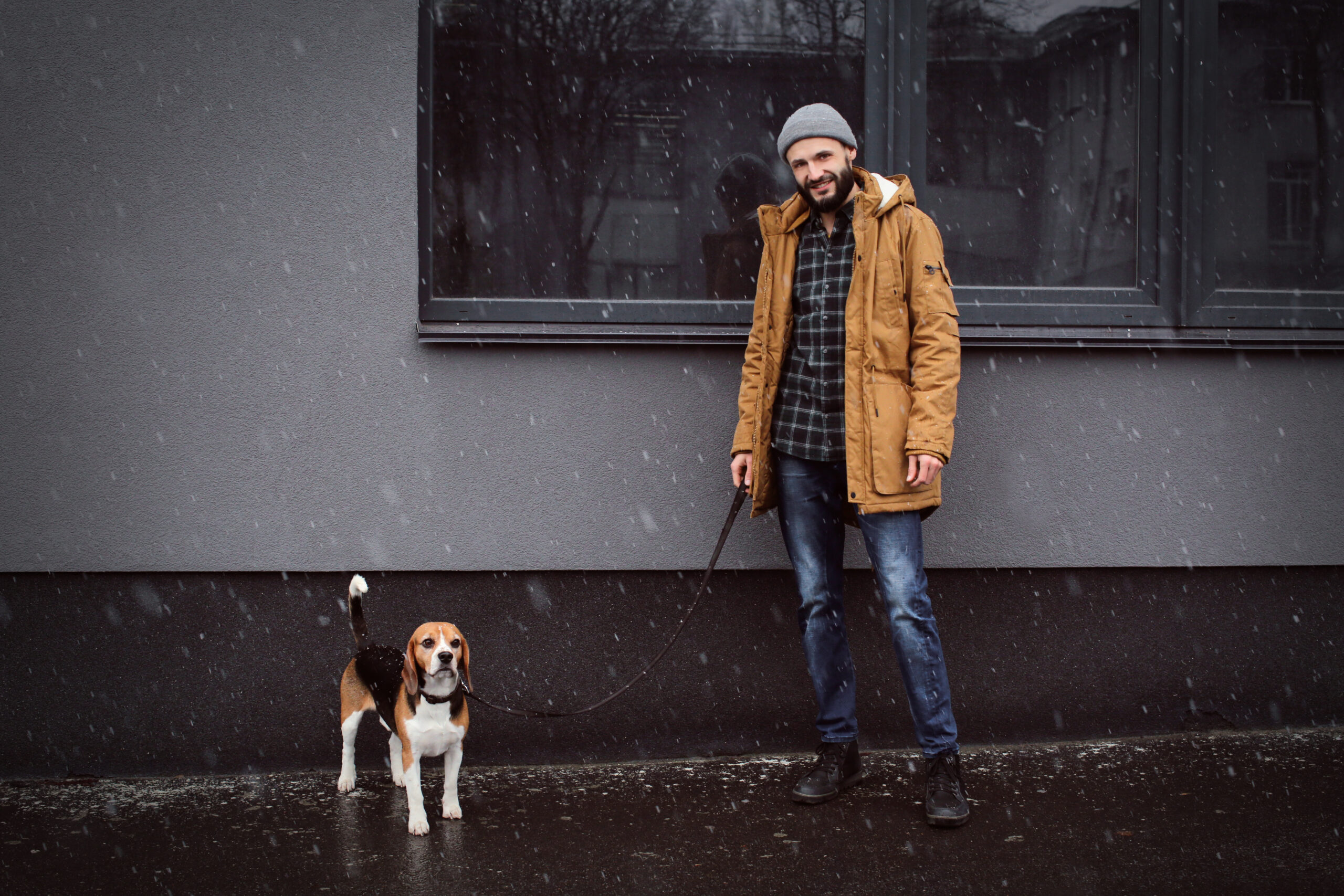 Handsome young hipster walking his dog outdoors on snowy day