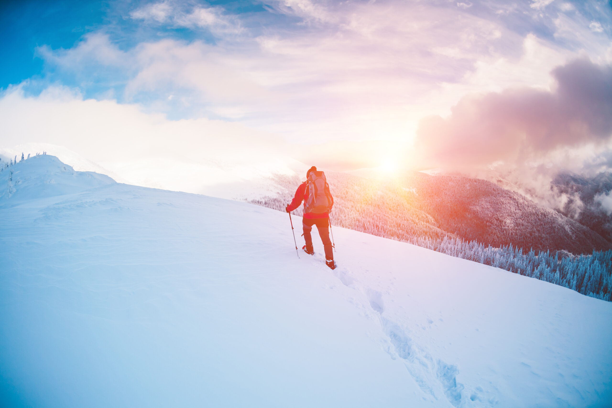 A man in snowshoes and trekking sticks in the mountains. Winter trip. Climbing of a climber against a beautiful sky with clouds. Active lifestyle. Climbing the mountain through the snow.