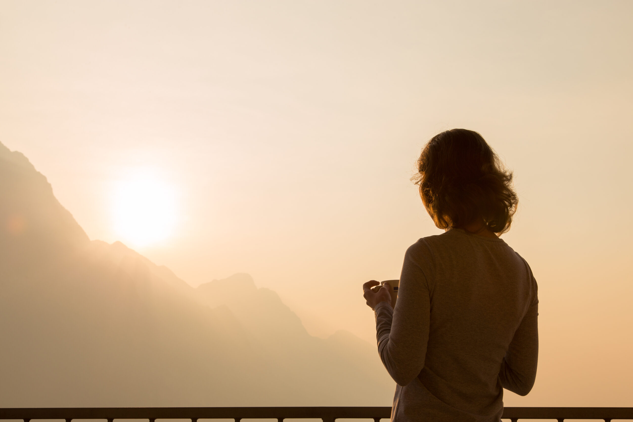 Woman traveler silhouette starting new day enjoying morning coffee looking at peaceful serene sunrise on morning sky watching sunlight above mountains landscape relaxing on travel vacation, rear view