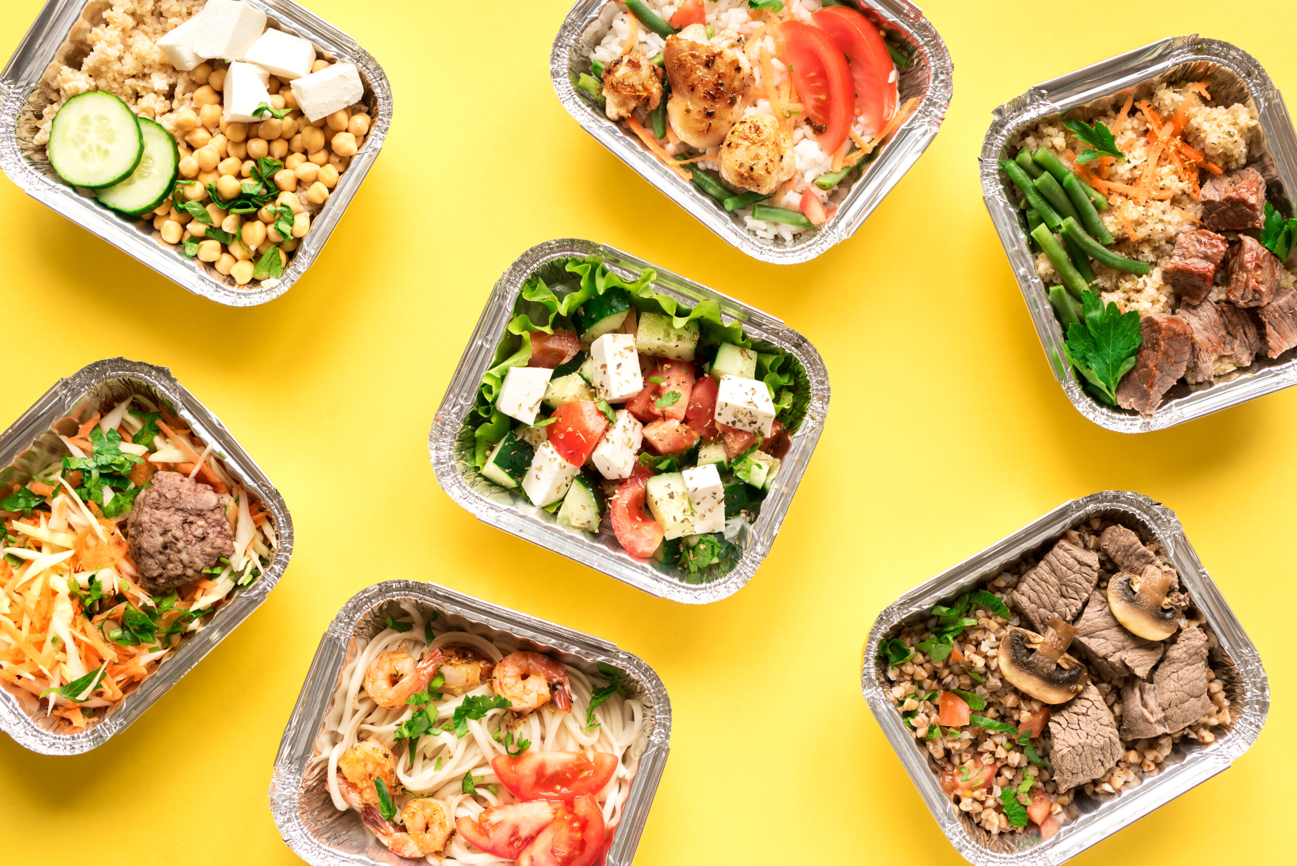 Daily meals in foil boxes on yellow background, top view, flat lay. Healthy food delivery concept. Fitness nutrition for diet.