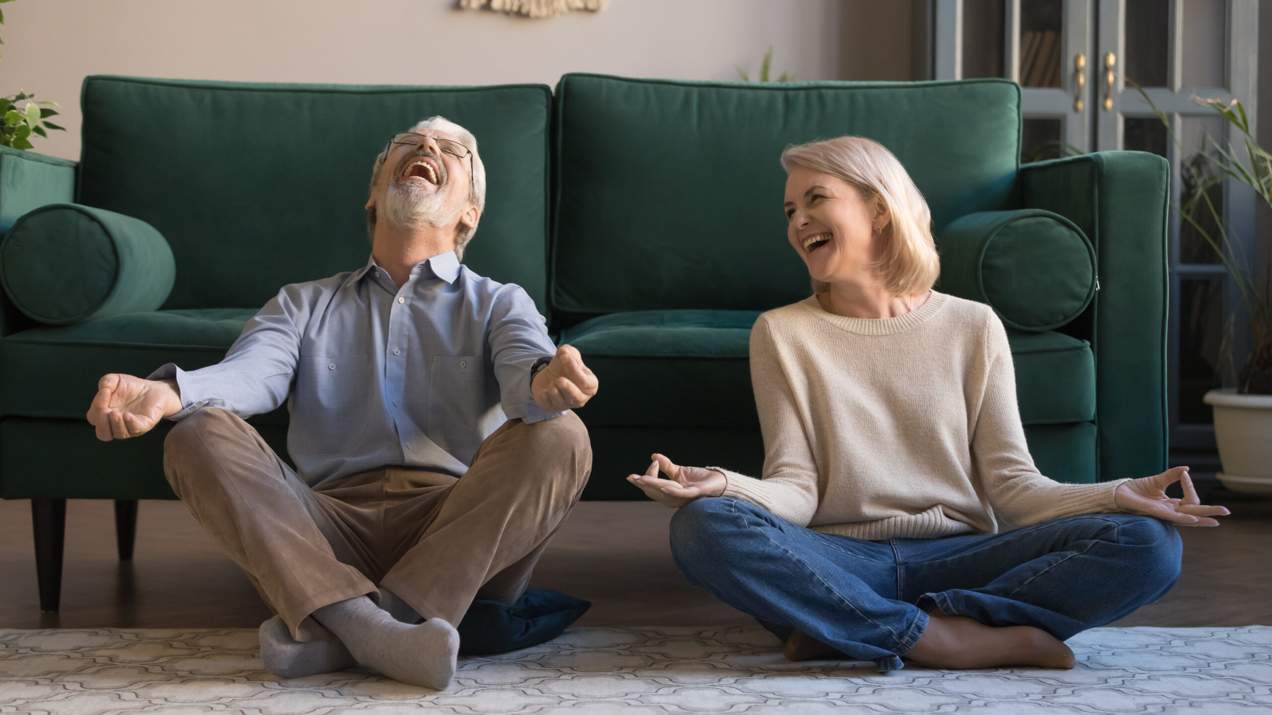 Laughing funny elderly spouses sitting in living room on floor in lotus position practice meditation distracted from yoga exercise joking feels overjoyed, healthy active lifestyle