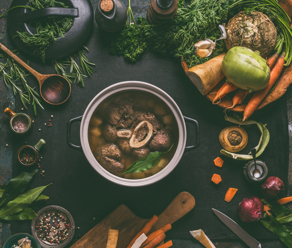 beef bone broth Cooked beef meat shin with bone in cooking pot on dark kitchen table background with low carb vegetables and spices ingredients for soup, top view. Meat broth or stock. Clean low-calorie food 