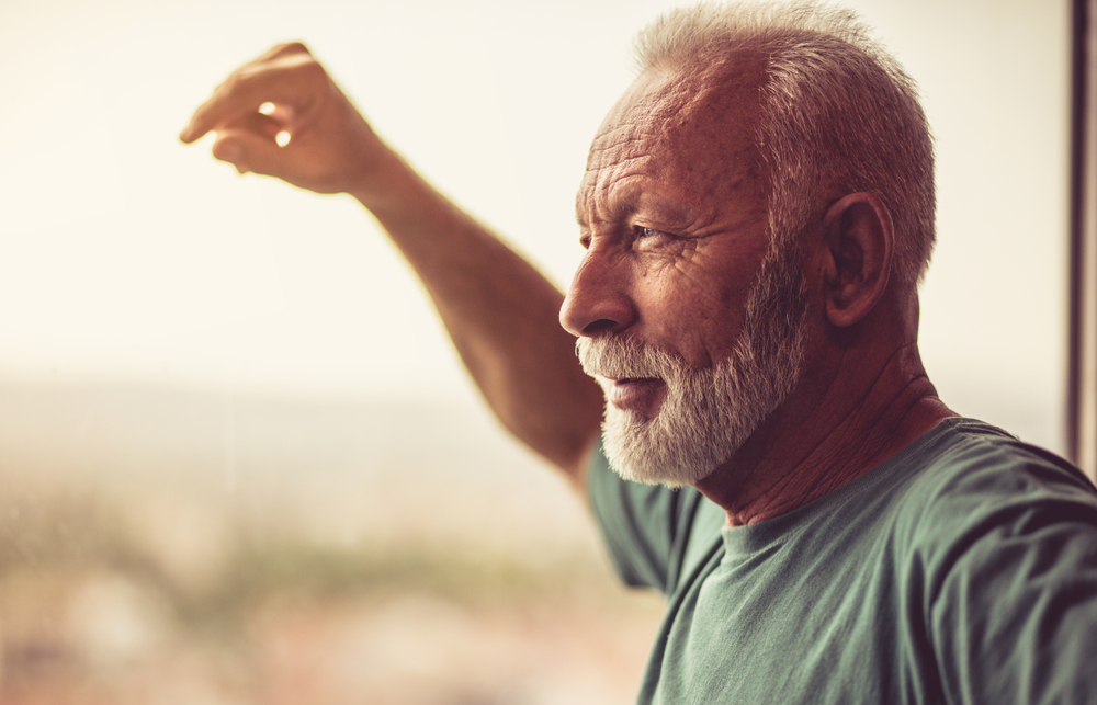 good day at home working out. Senior man standing next to the window after exercise. Looking away. Close up.