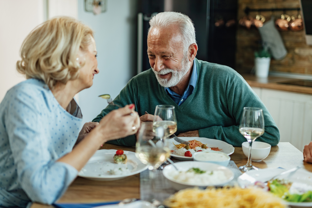 Eating for longevity Happy mature man and his wife talking while having lunch together in dining room.